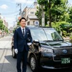 清潔感のあるタクシー車両の横で笑顔を見せるプロの運転手。自由な働き方をイメージした明るい都市景観