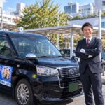 さいたま市の駅前で笑顔で立つ、清潔感のある制服姿のタクシードライバー