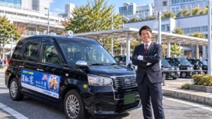 さいたま市の駅前で笑顔で立つ、清潔感のある制服姿のタクシードライバー